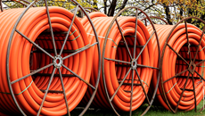 Three large reels of orange communication duct sit in the grass with trees in the background.